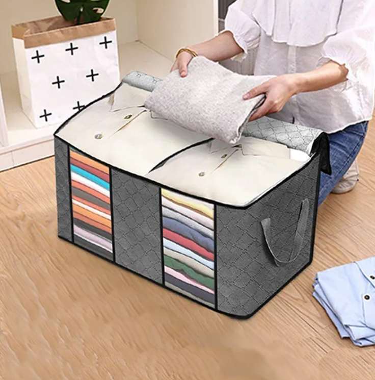Grey non-woven quilt storage bag with clear side windows being packed with folded bedding on a timber floor